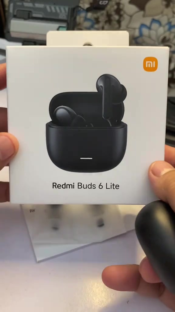 Kotak Redmi Buds 6 Lite dengan gambar fon telinga dan bekas pengecas, dipegang tangan