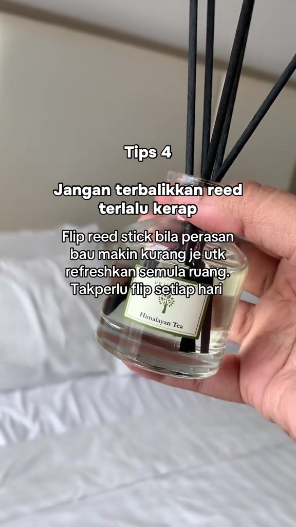 Tangan memegang botol reed diffuser dengan batang reed hitam