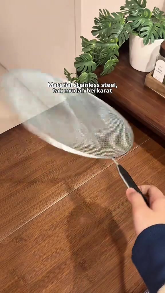 Penutup kuali jaring diangkat pada pemegangnya di atas meja dapur.