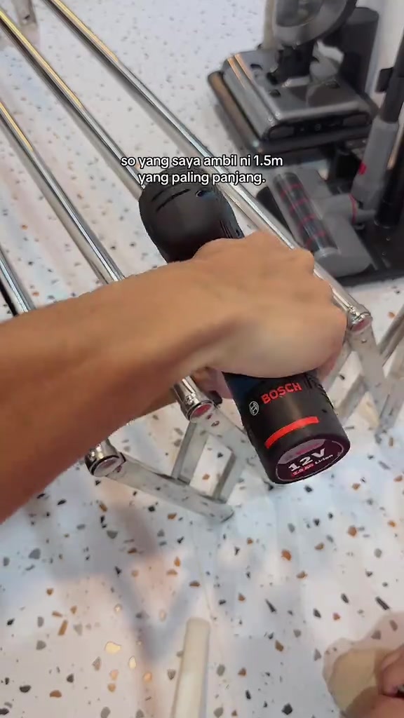 Tangan memegang drill ketika memasang rel ampaian pada dinding