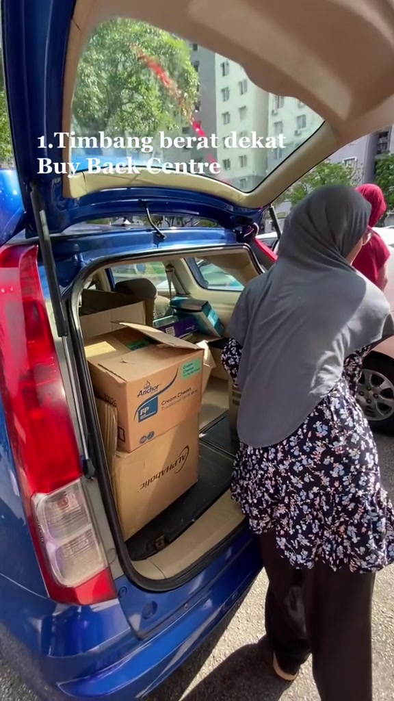 Seorang pengunjung dari belakang membawa kotak ke kereta di pusat kitar semula