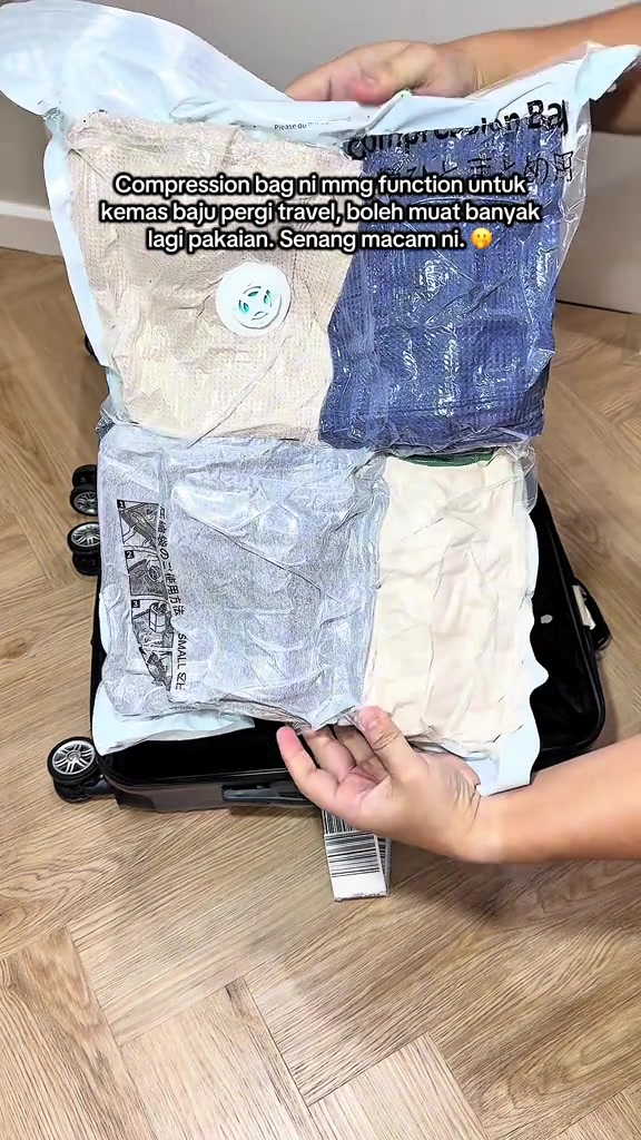 Tangan memegang beberapa beg mampatan pakaian di atas luggage terbuka